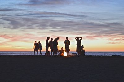 group of people gathered around a campfire at the beach